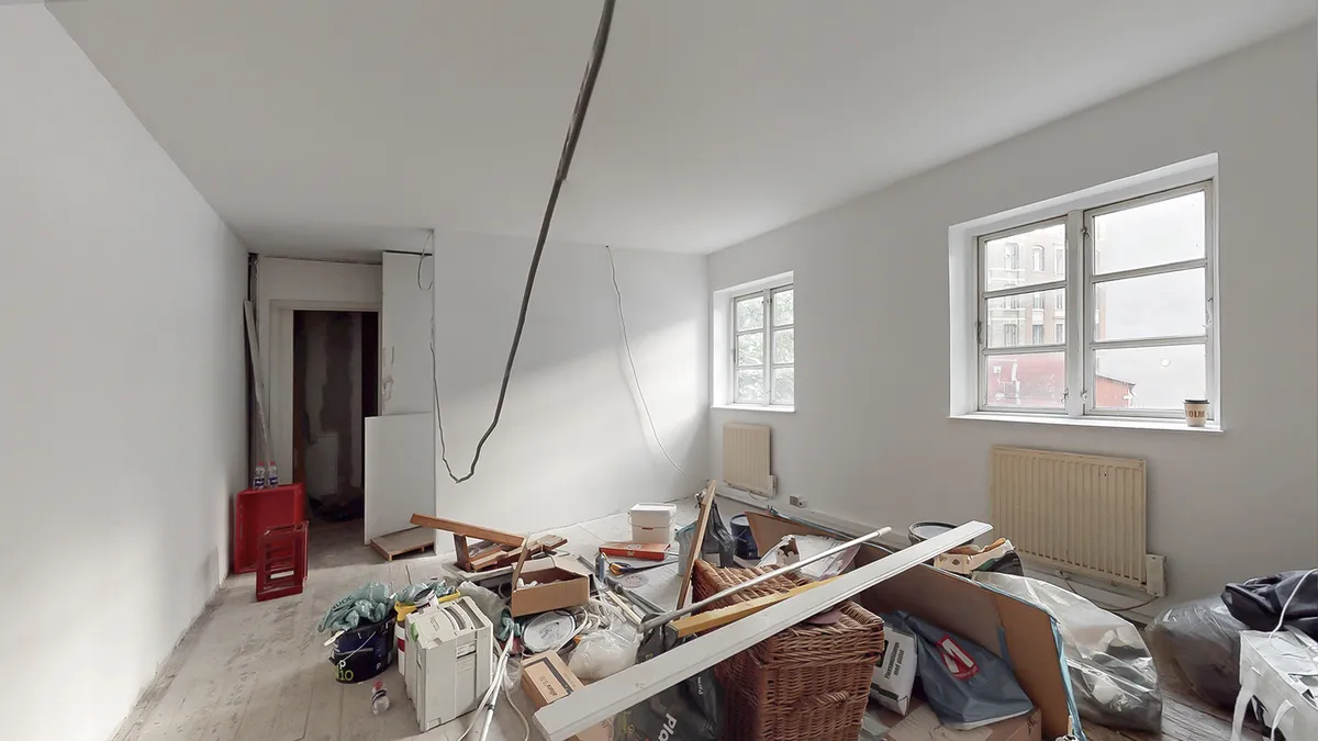 Rum med hvide vægge, loft og gulv samt flere genstande, kartoner og en kaffekop på vindueskarm