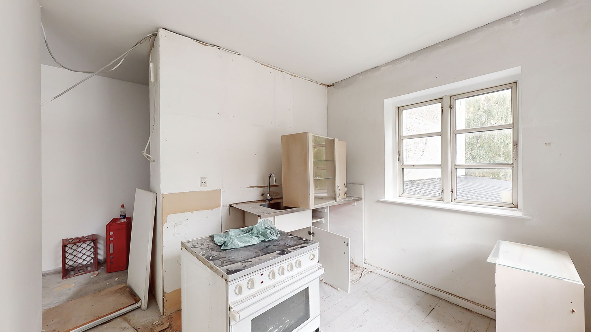 En renoveret køkken med ovn, vaskebækken og et skur med en kasse og en flaske i et lejlighedshus