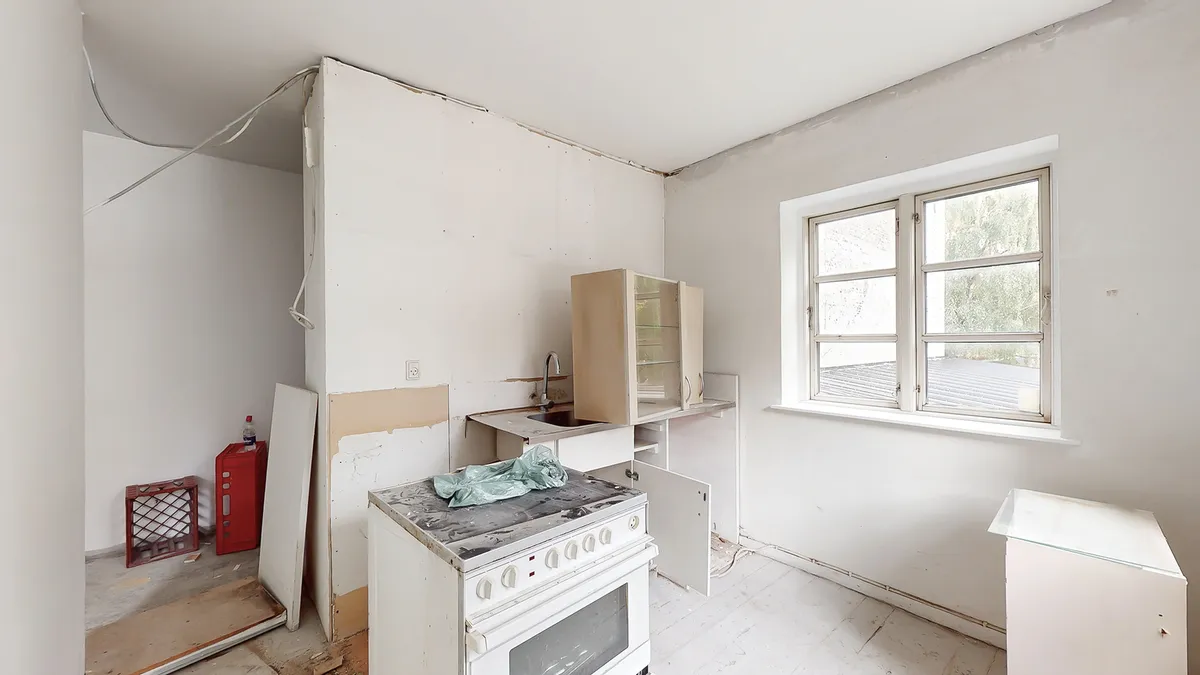 En renoveret køkken med ovn, vaskebækken og et skur med en kasse og en flaske i et lejlighedshus