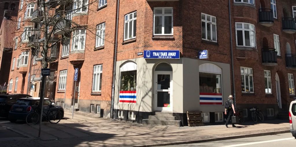 Take-Away med rødt og hvidt Thai flag, hvor en mand går med en rygsæk og en taske