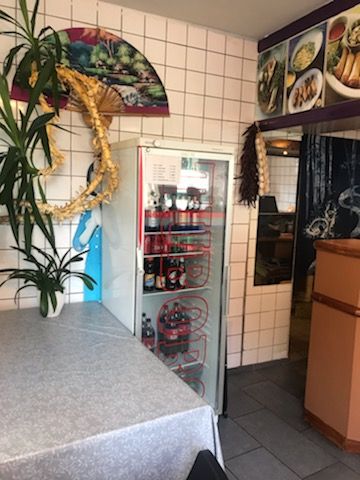 Take-Away forretning med en køleskab med drikkevarer, et bord med en plante og et vindrullende dør og en væg med eksotiske