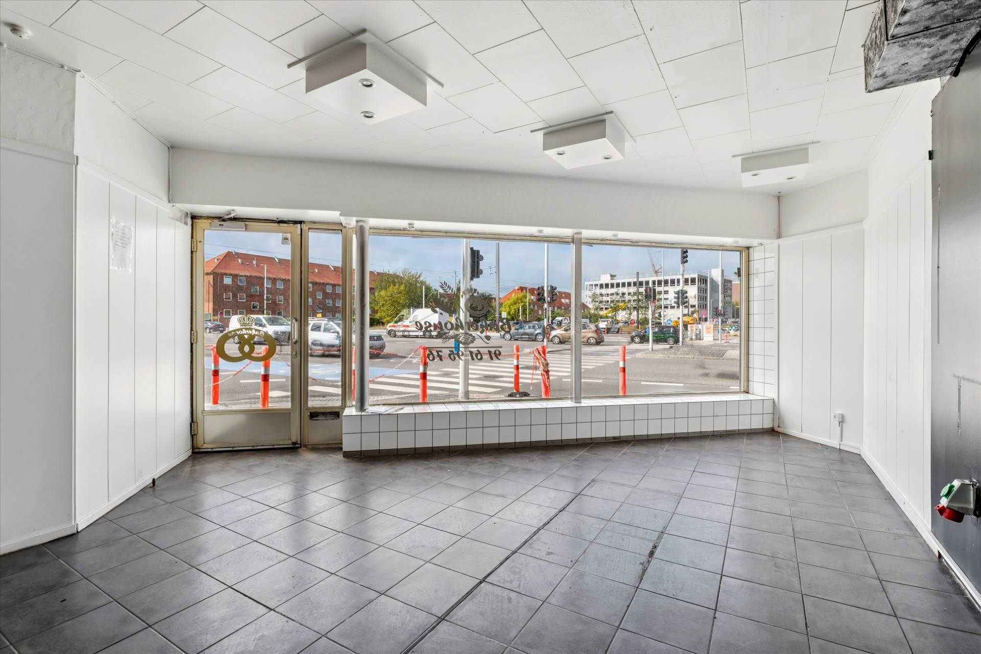 Lejemål med store vinduer og enkle interiører, der giver gode muligheder for butik eller kontor. Bygningen med facade og