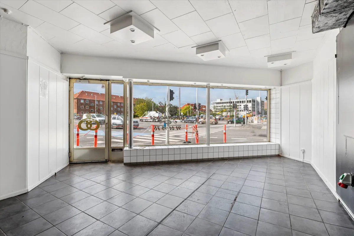 Lejemål med store vinduer og enkle interiører, der giver gode muligheder for butik eller kontor. Bygningen med facade og