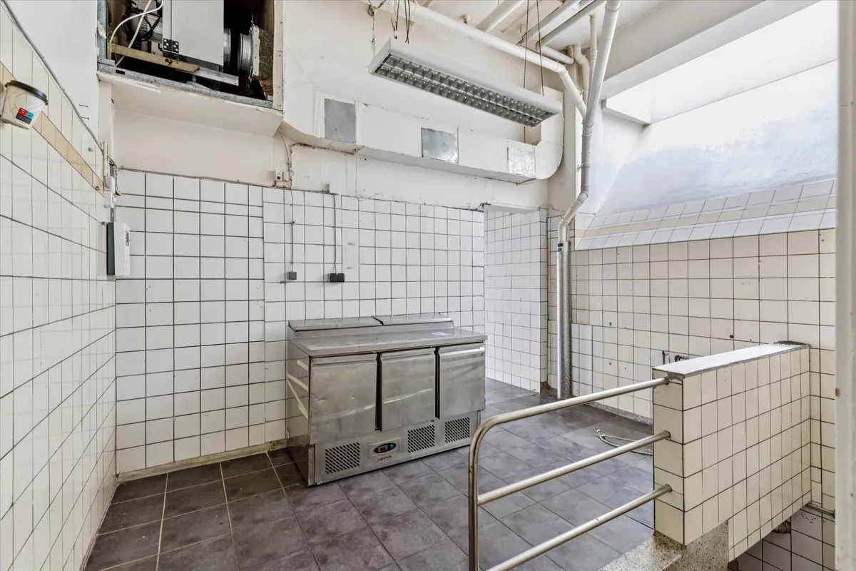 Køkken med højloft og metalkøleskab samt håndtag og hvidt klethedspanel i en kommerciel bygning