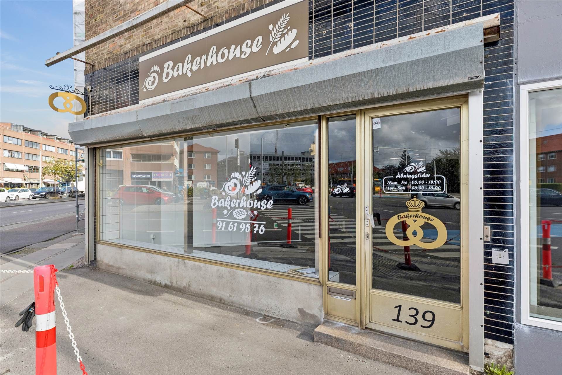 Bagerhus i Glostrup, forretning med adressenummer 139. Regnskærm og glasdør med åbningstider og telefonnummer. Parkerede