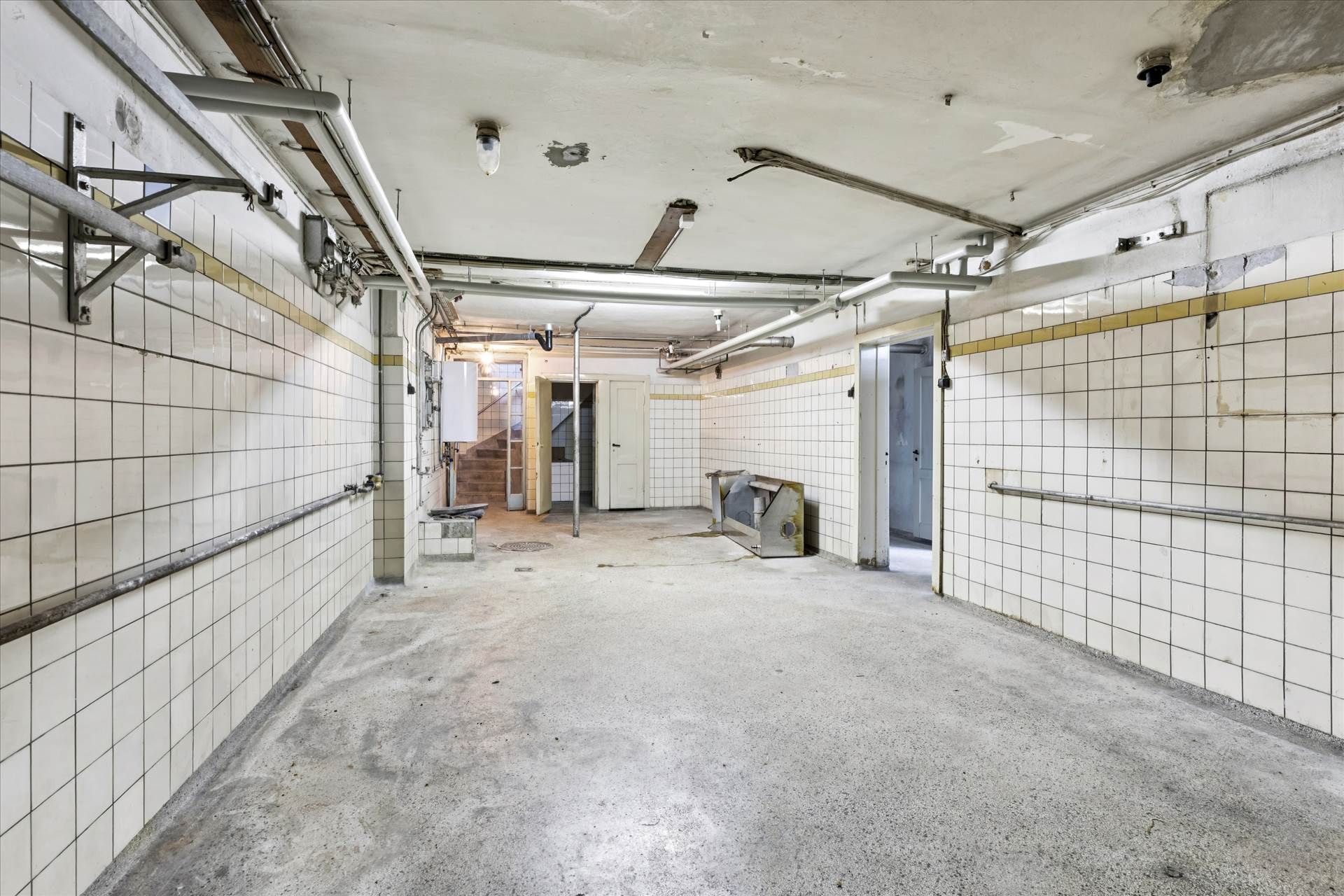 En stor, tom garage med to huse i baggrunden, hvor der er røg på loftet og røde og hvide klinker på væggene