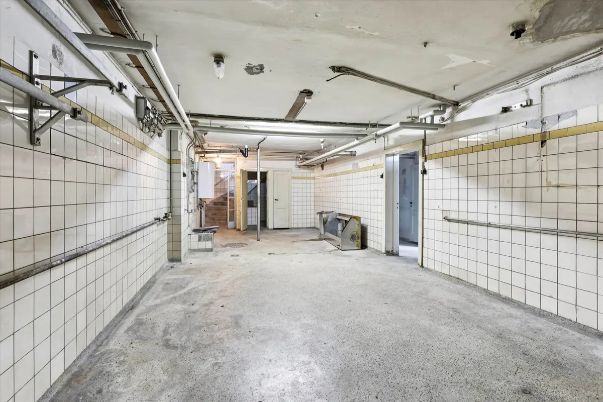 En stor, tom garage med to huse i baggrunden, hvor der er røg på loftet og røde og hvide klinker på væggene