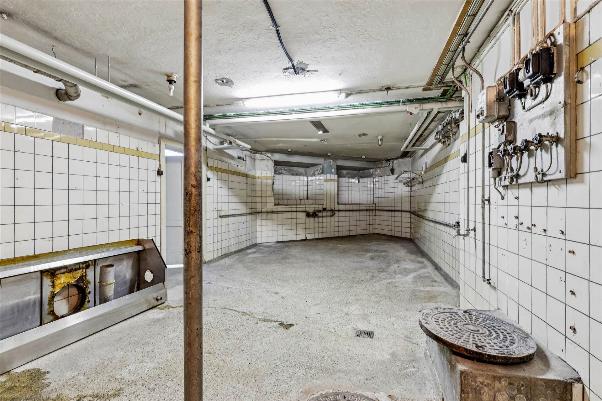 Rummeligt lokale med 63 m² stueplan og 92 m² kælder, hvor gulve og vægge er fliserne og rørledninger er synlige