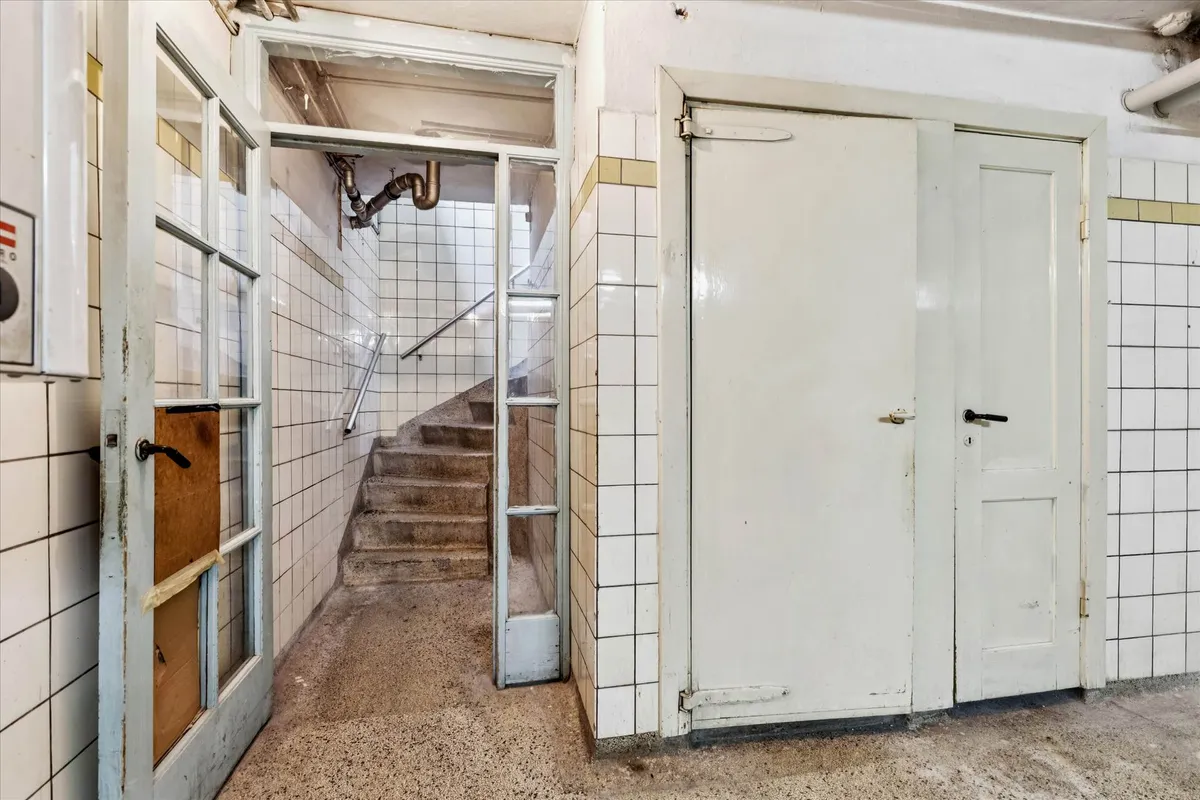 Lejemål med åbne døre, trappe og håndtag, formodentlig til en underjordisk indgang, i et tidligere badeanstalt.