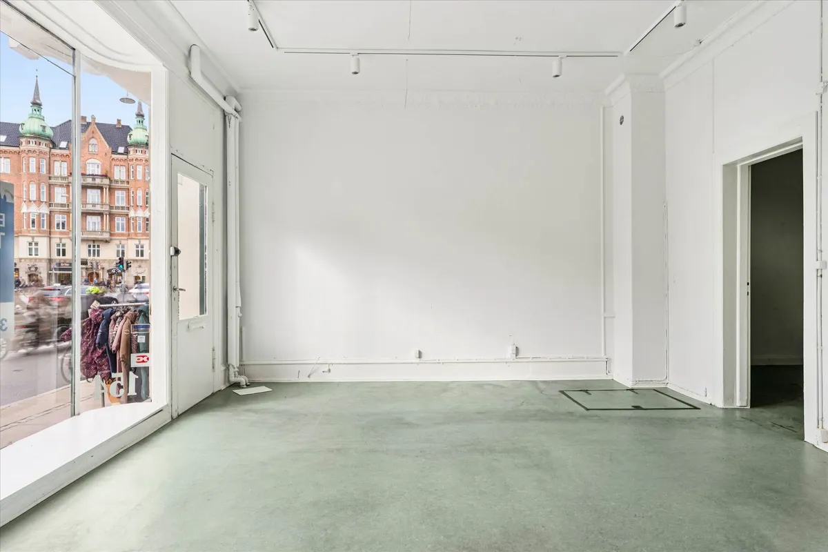 Et tomt lokale med 70 m² på stueplan og 20 m² i kælderen. Lokalet er i hjørnet og har store glasvinduer og trægulv.