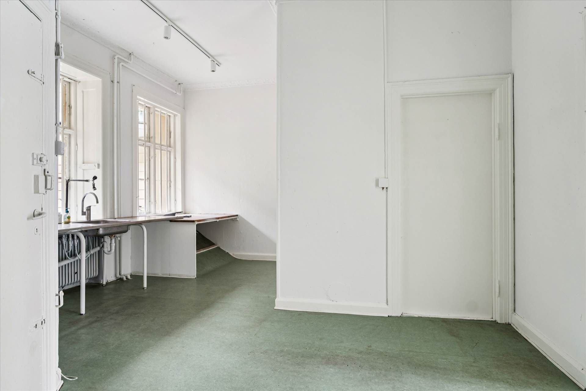 En tom hvid stue med hvide vægge og grønt gulv samt en stor dør og et vindue