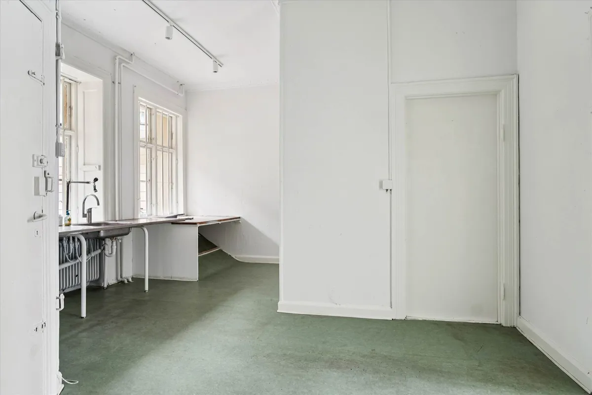 En tom hvid stue med hvide vægge og grønt gulv samt en stor dør og et vindue