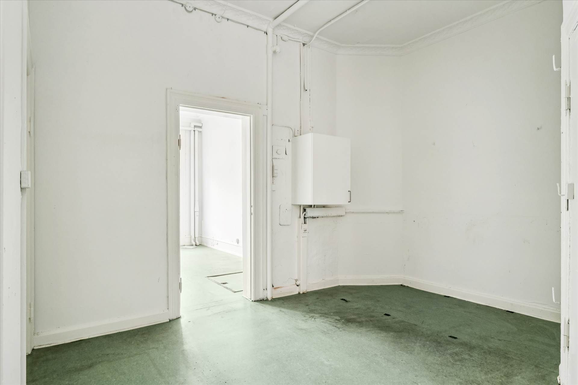 Tomt og rent butikslokale med åbne døre og lyse, grønne gulve i en hvid farvetone.