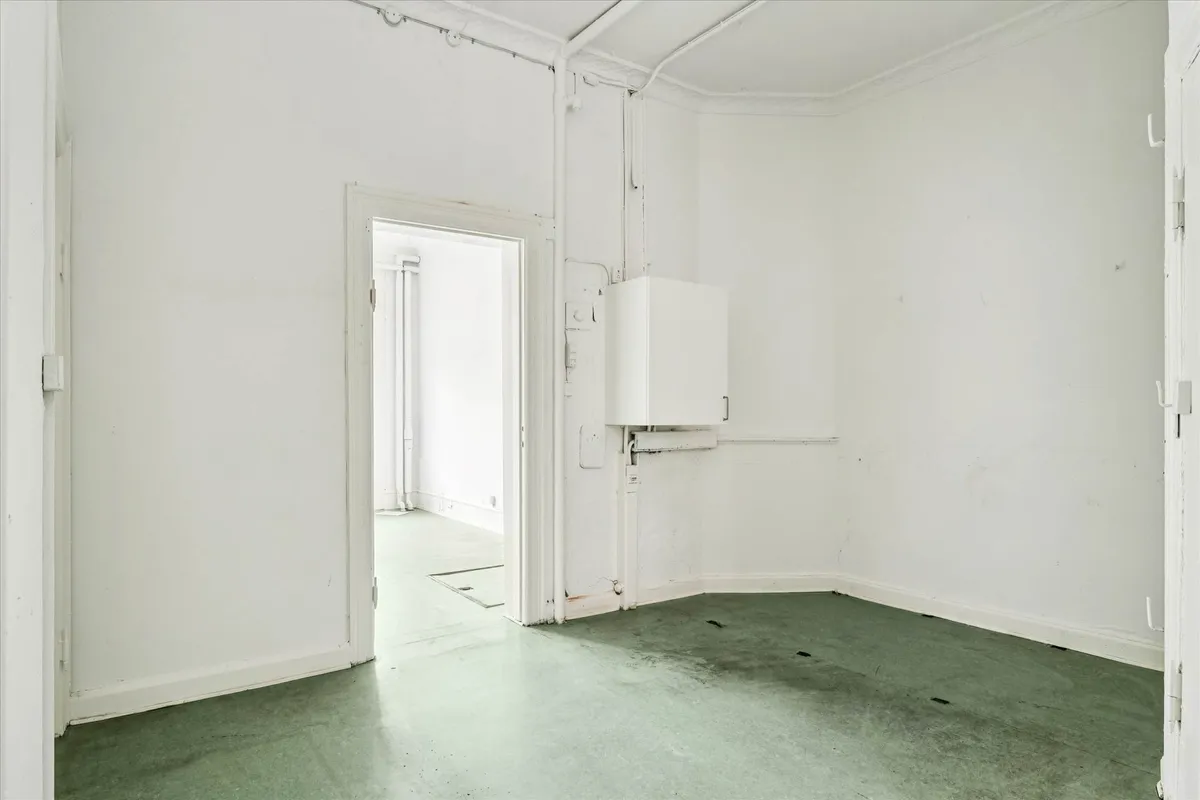 Tomt og rent butikslokale med åbne døre og lyse, grønne gulve i en hvid farvetone.