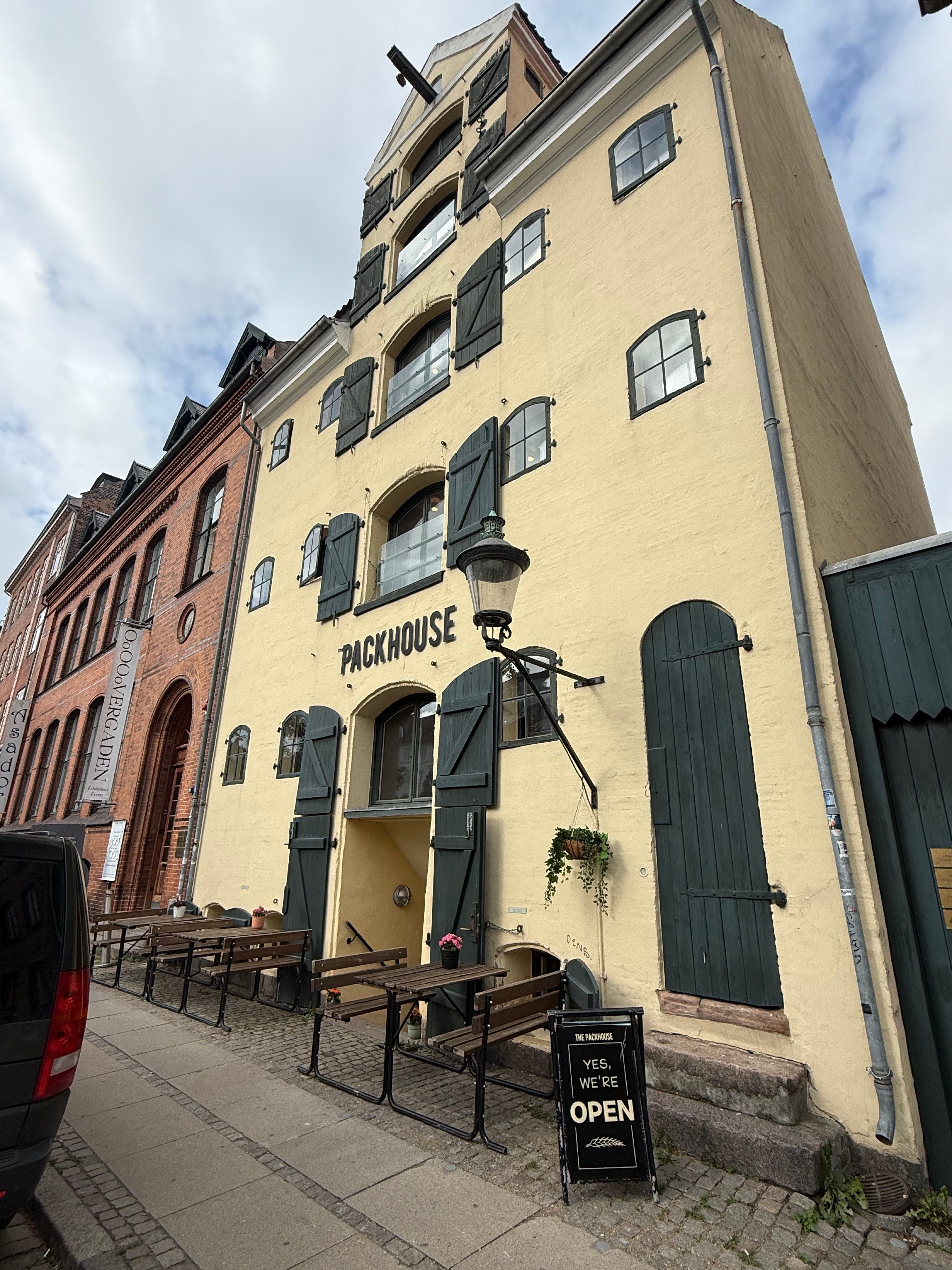 Forretningslokaler med grønne døre og vinduer på Christianshavn. Der er en søjle med en lampe og en plante. Der er træbænke