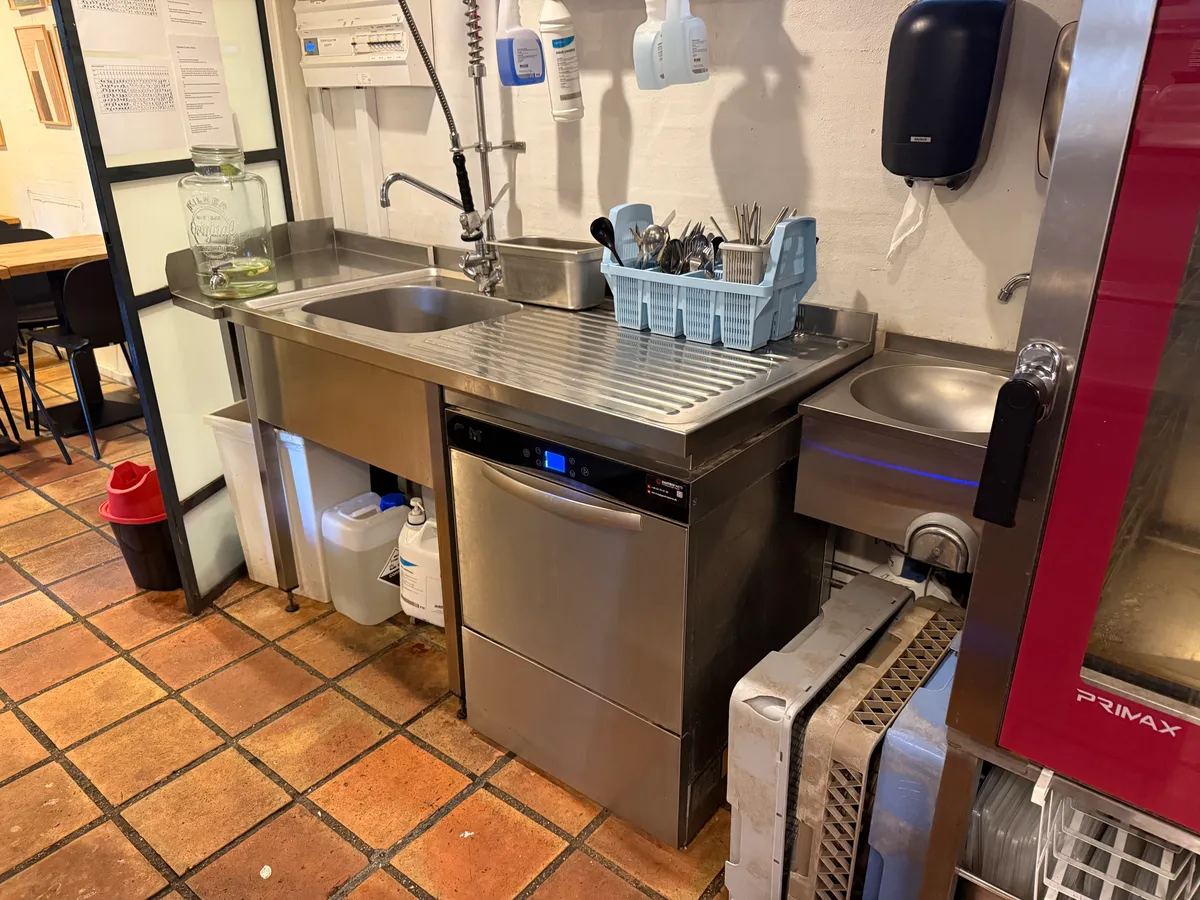 En ren og veludstyret køkkenforplejningsrum med dobbelt vask, opvaskmaskine og børsteholder. En glasurbeholder og en