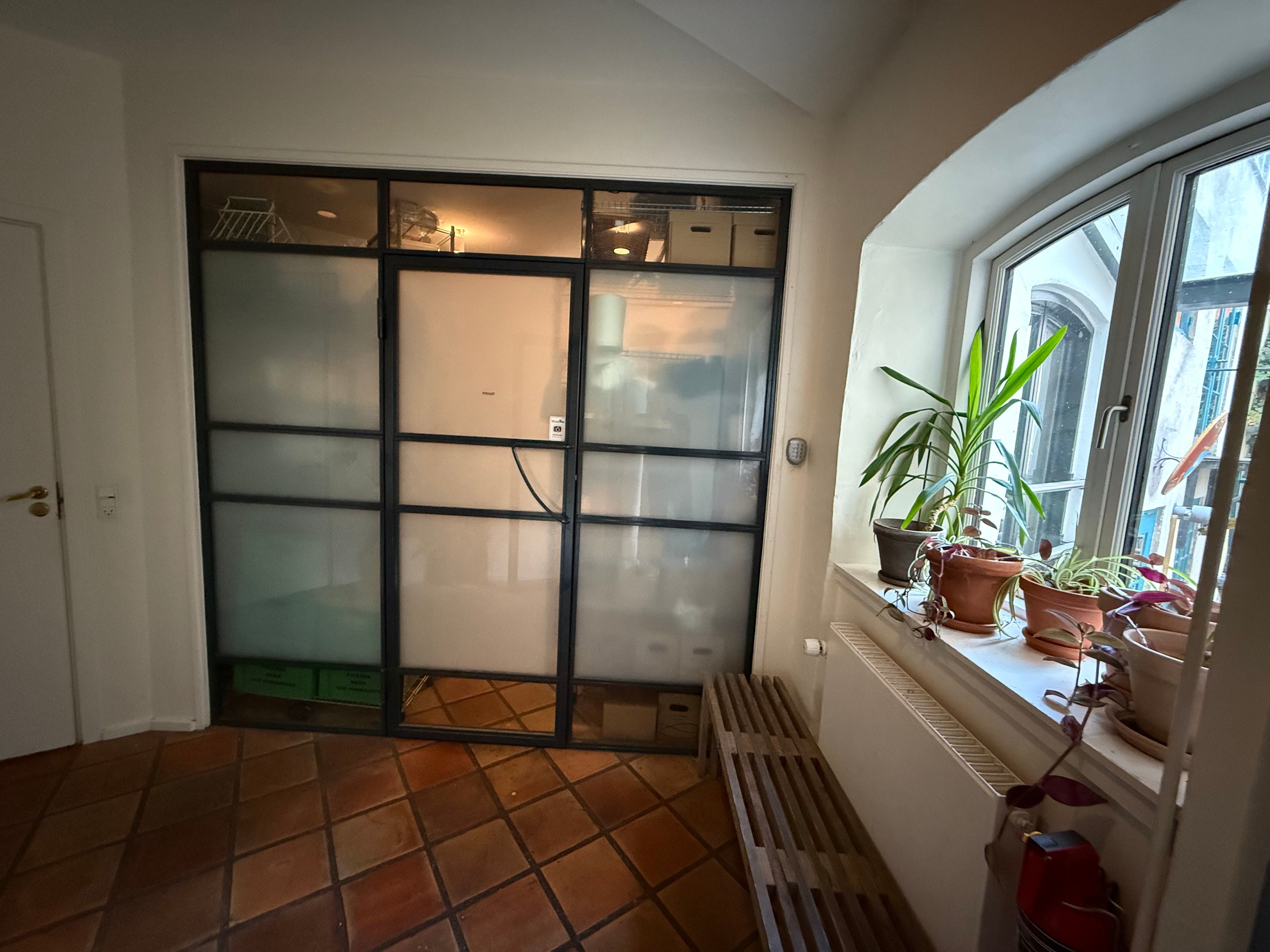 En rummelig stue med lysegul gulvbeklædning og en stor vinduesbank med flere potter og planter