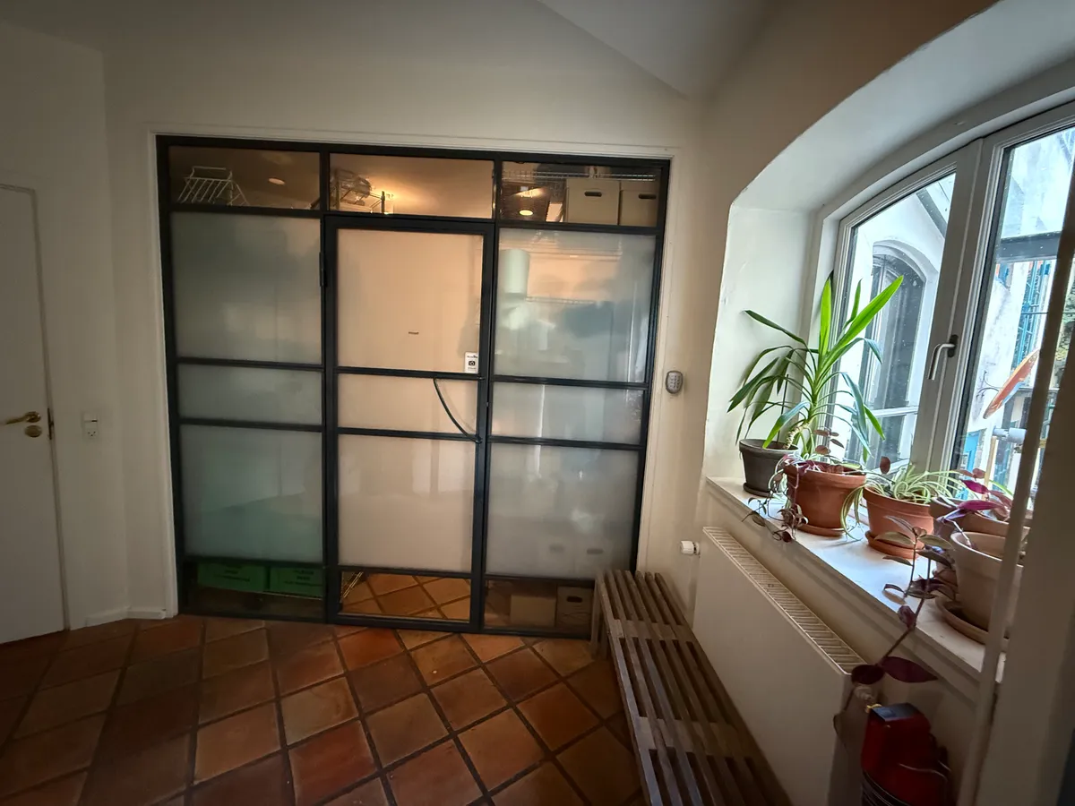 En rummelig stue med lysegul gulvbeklædning og en stor vinduesbank med flere potter og planter