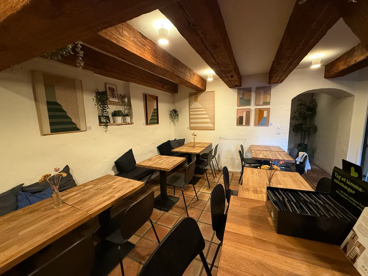 En lækker restaurant med træborde og stole, loftsbjælker og moderne kunstværker på væggen, samt en blomster i en vase