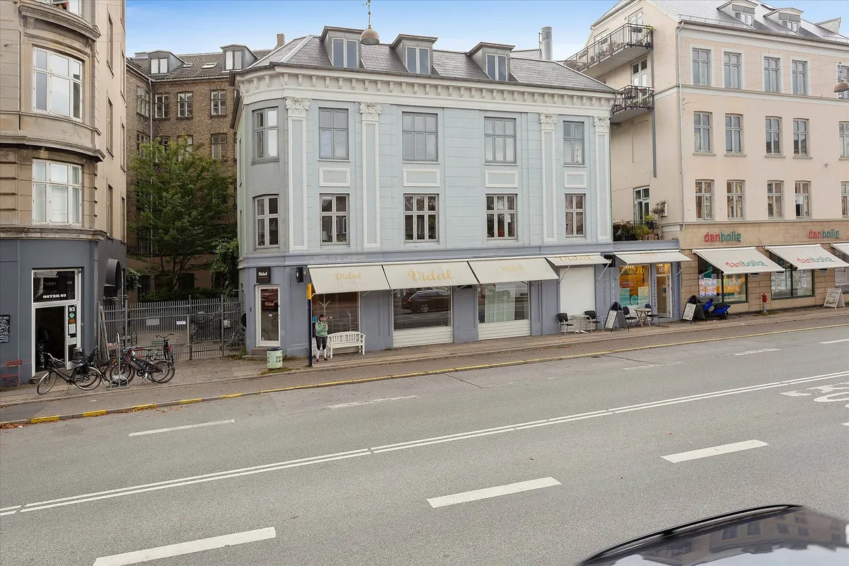 Facaden af en butik på Øster Farimagsgade, med glasvinduer, hvide vægge og lysegul gulv. Butikken har en hvid sofa og bord