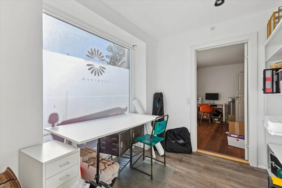 Studie med højloft, hvidt bord, to stole, stol med blåt sæde og en sort taske på gulvet