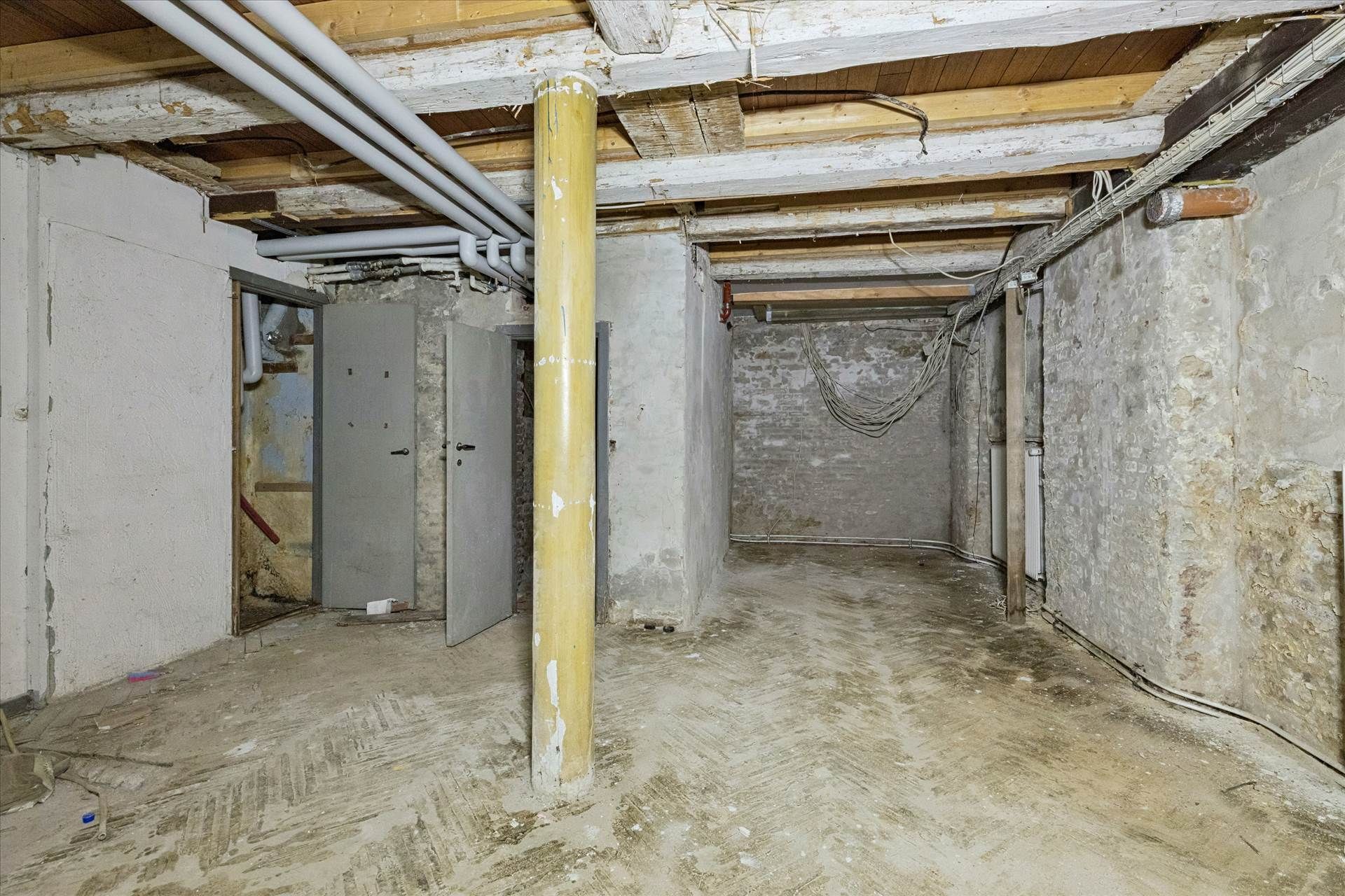 En tom underjordisk lagerrum med højt til loftet, gamle, røde mursten og to metalliske døre.