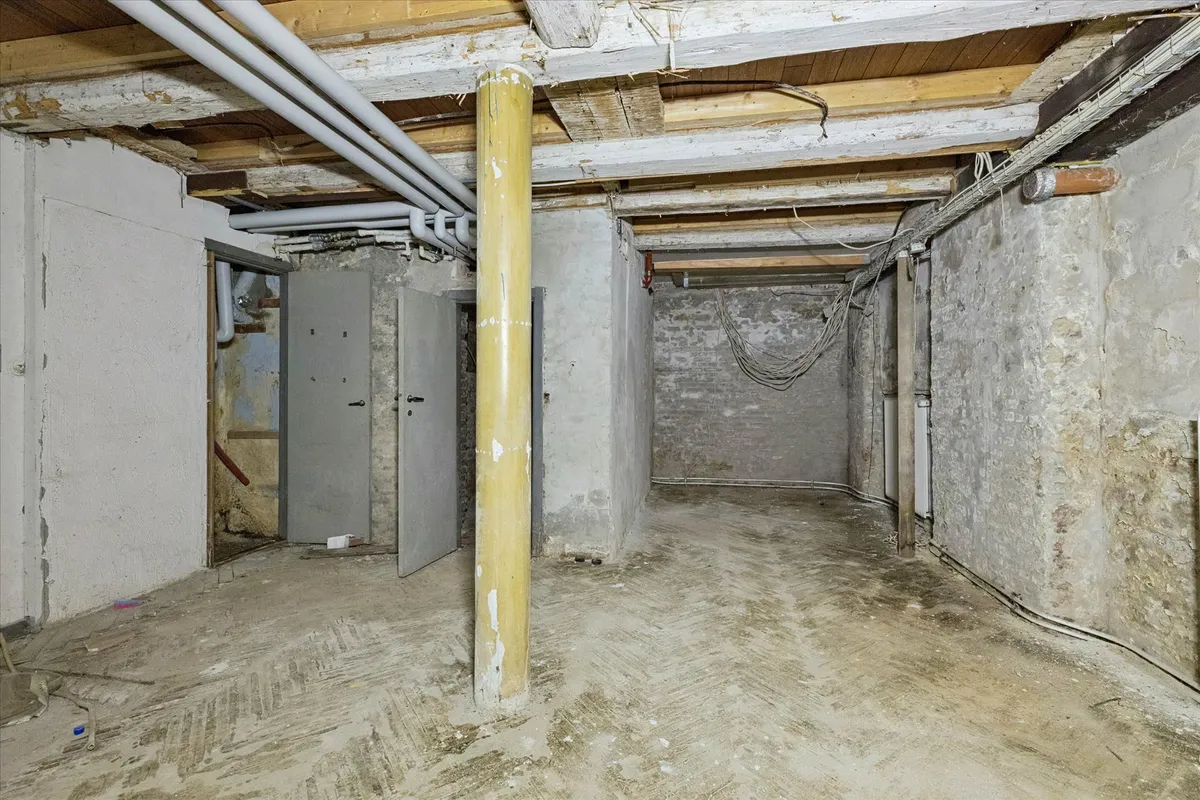 En tom underjordisk lagerrum med højt til loftet, gamle, røde mursten og to metalliske døre.