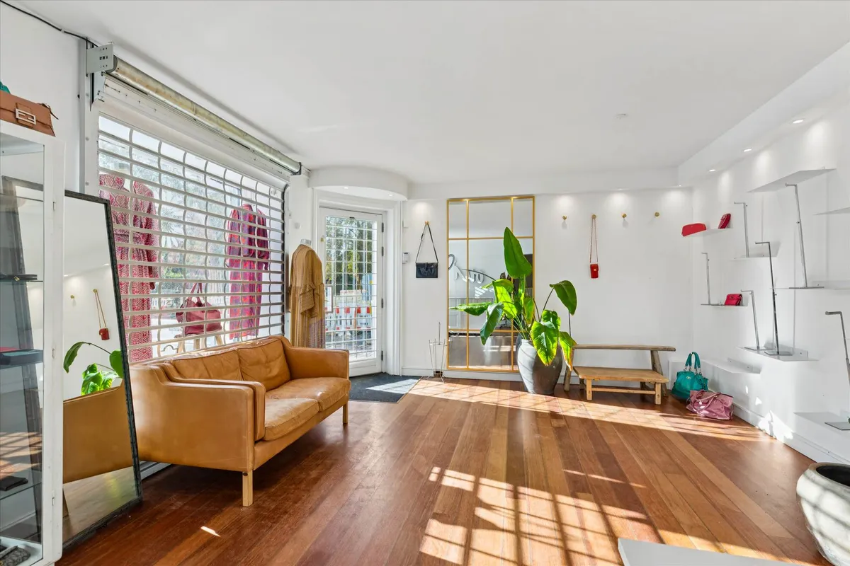 Elegant indretning med lyse trægulve, højloft, og et stort spejl samt en sofa med lyse læder. Der er også et gulvmøbleret