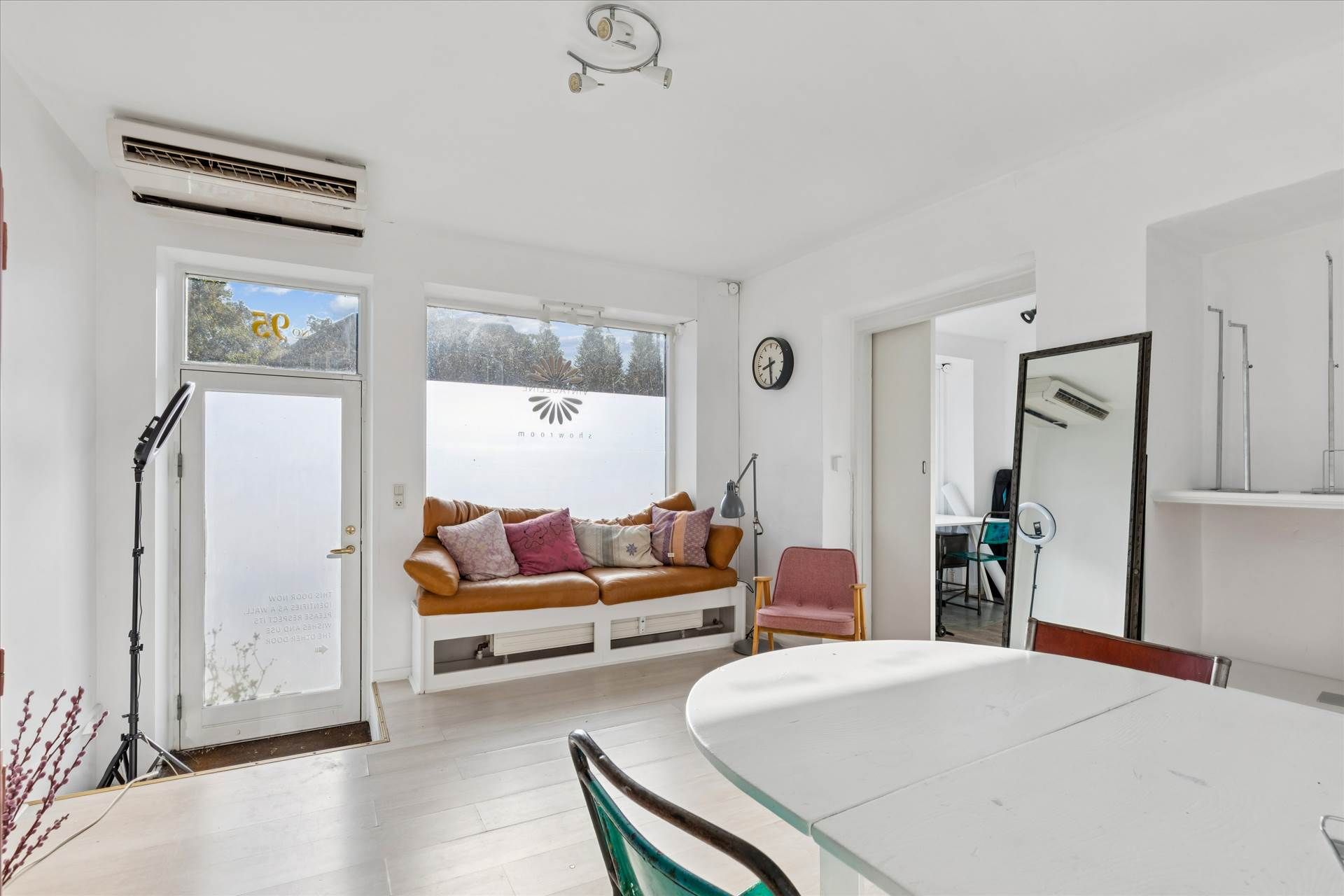 Butik med åbent vinduesparti og lædersofa med puder, lysarmatur, klokke og spejl i en hvid indretning