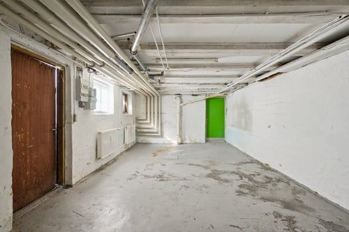 Lagerrum med træ- og grøndør, radiatorer og lyse gulv og vægge i et tidligere industriområde