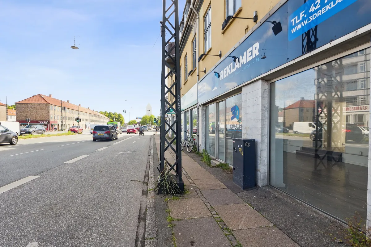 En butik med navnet Reklamer på en travlt trafikeret gade med biler og folk som passerer