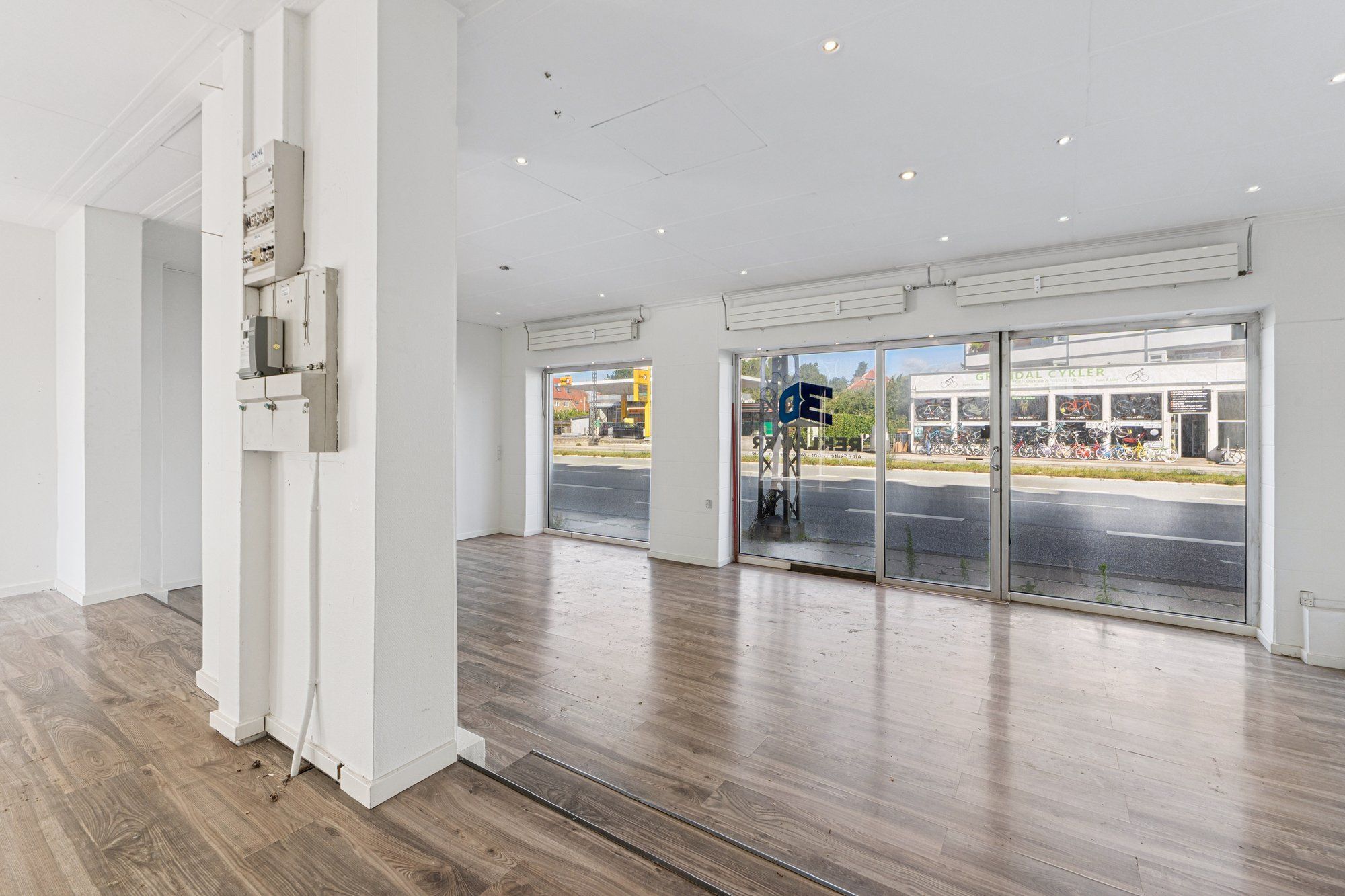 Køkken med højloftede rum og krydsfinergulve, åbne glasdøre med udsigt til gaden med grønne områder og parkerede cykler