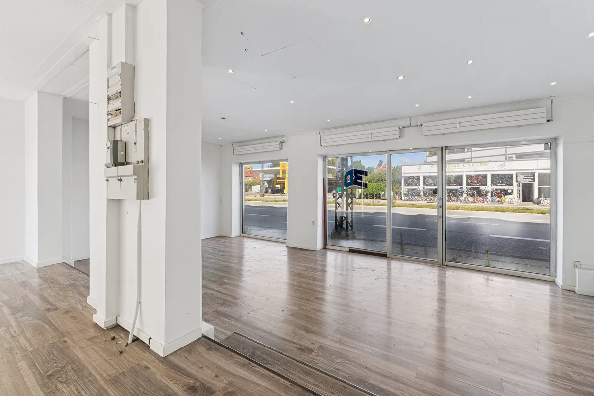 Køkken med højloftede rum og krydsfinergulve, åbne glasdøre med udsigt til gaden med grønne områder og parkerede cykler