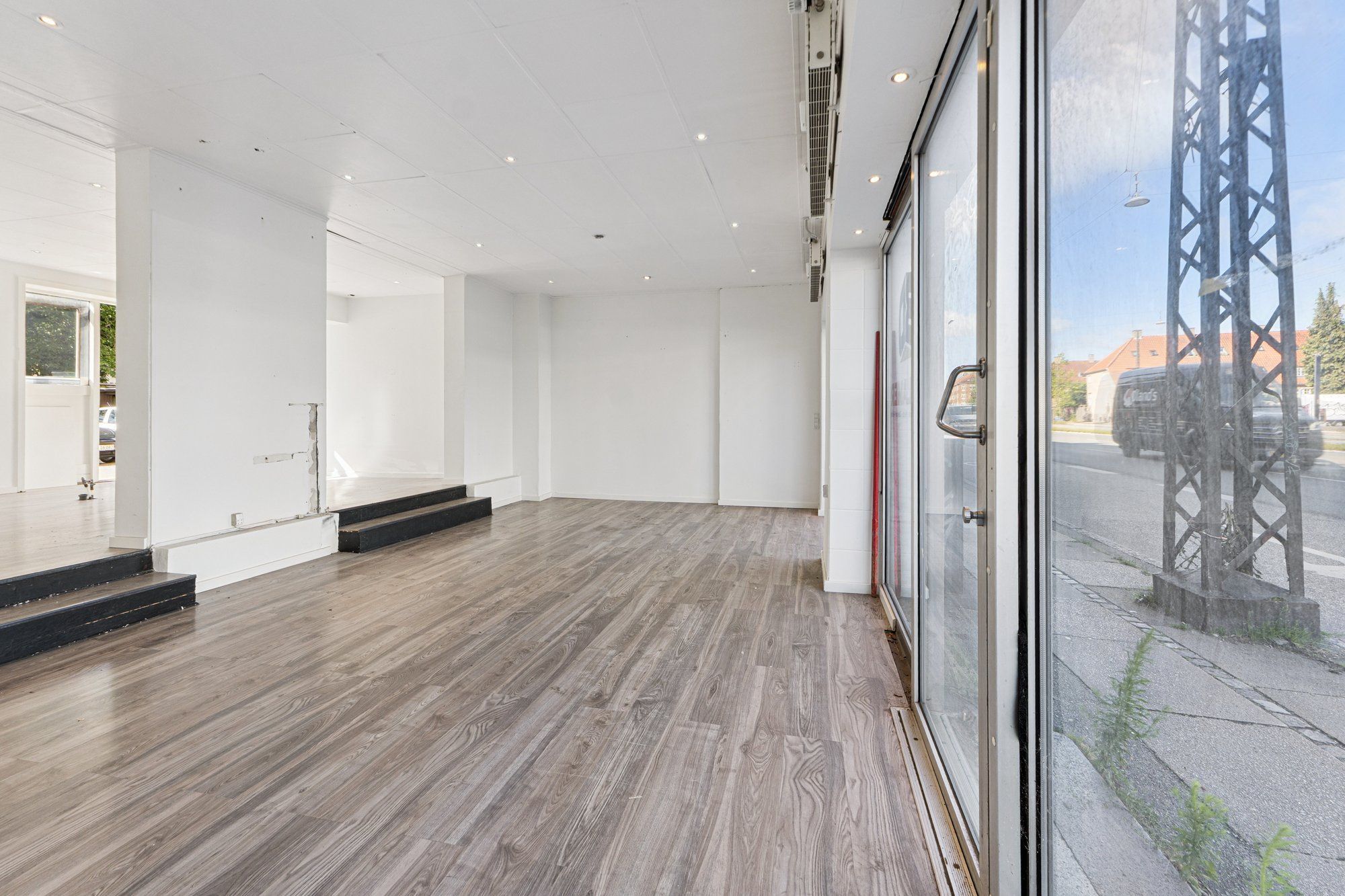 En stor glasdør i en stor, møbleret, tom stue med hårdt gulv og smukke hvide vægge og loft