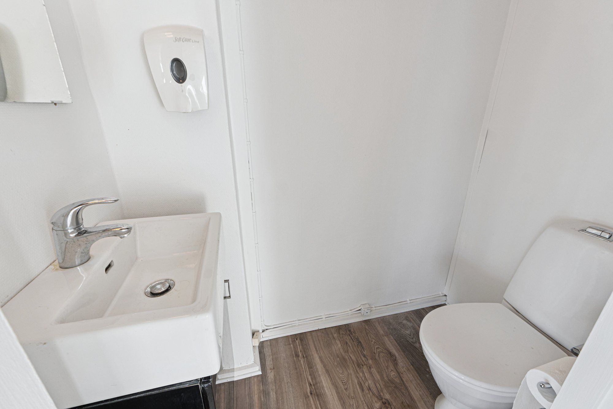 Et lille badeværelse med hvide vægge, en hvid toilet, et hvidt vasketøjsbælte og en hvid håndvask med en sølvfarvet vandhane