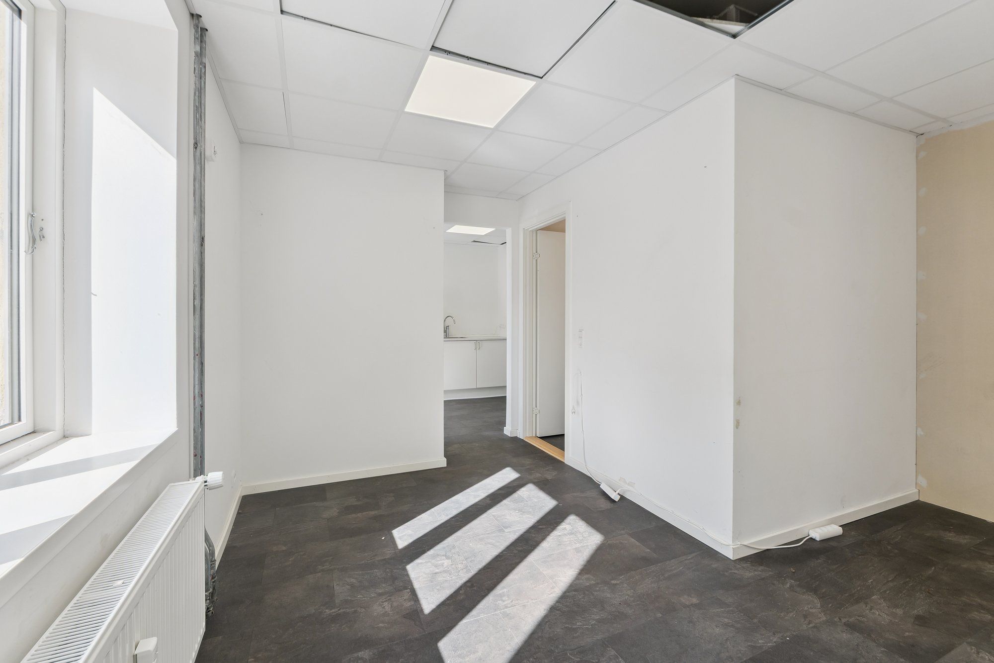 Minimalistisk, ren og hvidt dekoreret rum med et moderne loft, solskin og en radiator under et vindue