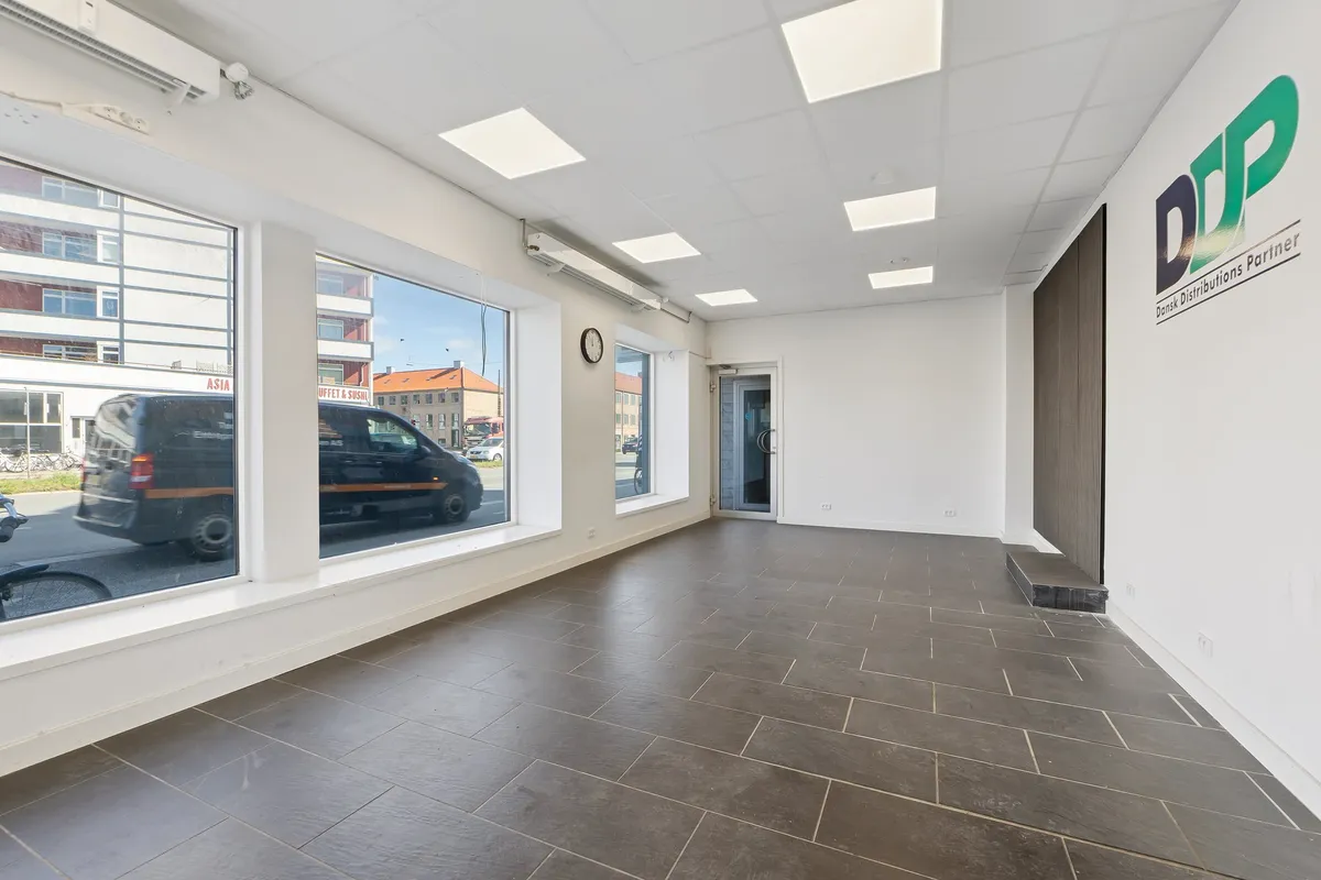 Her ses et kontor med vinduer, en dør, en simpel indretning, lyse loftsplader, et klokkeskilt og en vægmaling.