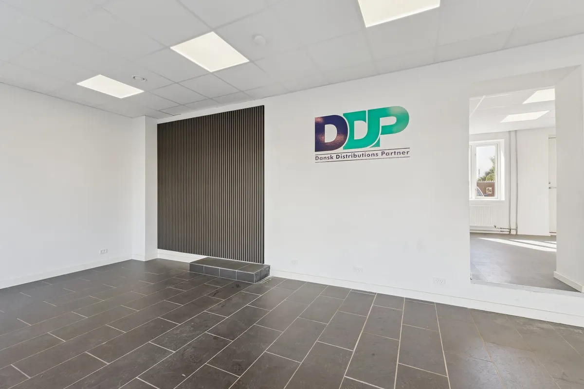 Indenfor et hvidt kontor med tavle med DDP tekst og logo og en sort skrå tavle. Gulvet er lysegrå og loftet er hvidt med