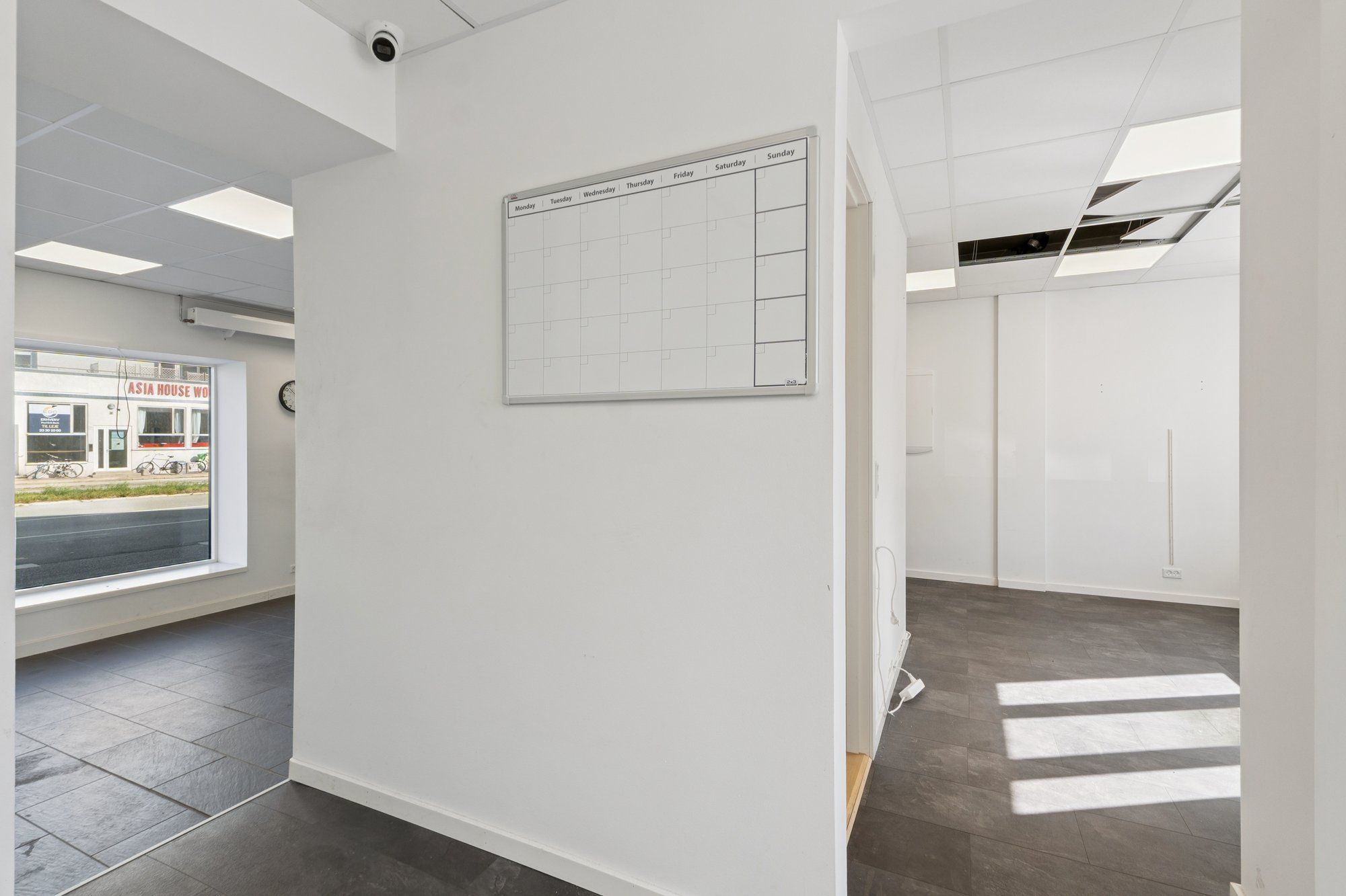 Magtfulde kontorlokale med hvide vægge, højloft, kalender, surveillance kamera og glasvindue med udsigt til en bygade