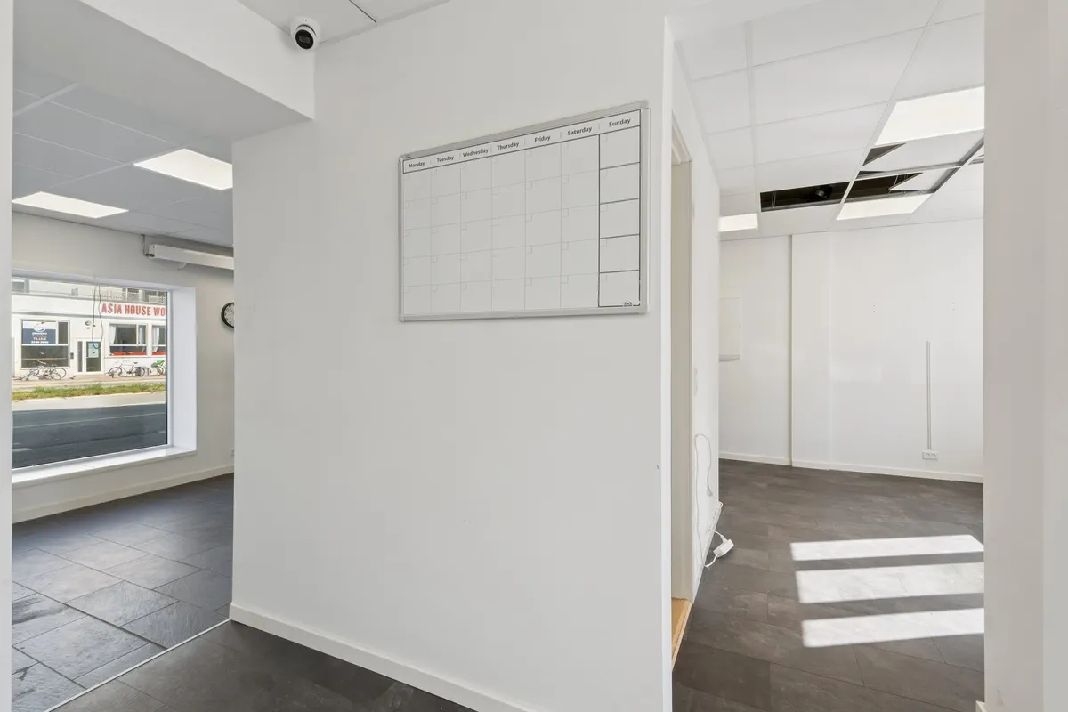 Magtfulde kontorlokale med hvide vægge, højloft, kalender, surveillance kamera og glasvindue med udsigt til en bygade