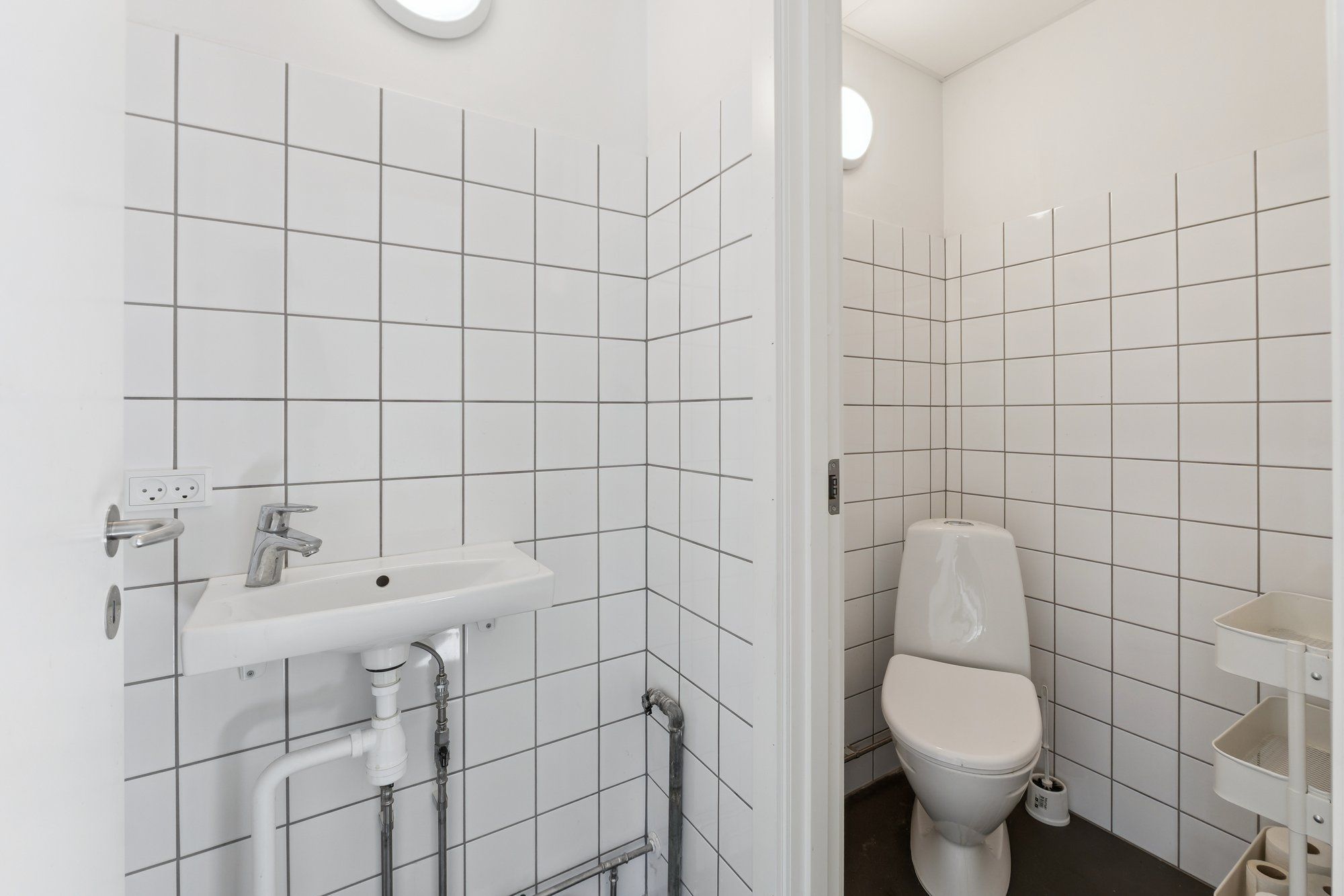 Et rent badeværelse med en hvid toilet, hvid vask og en stor spejl samt hvide flisede vægge