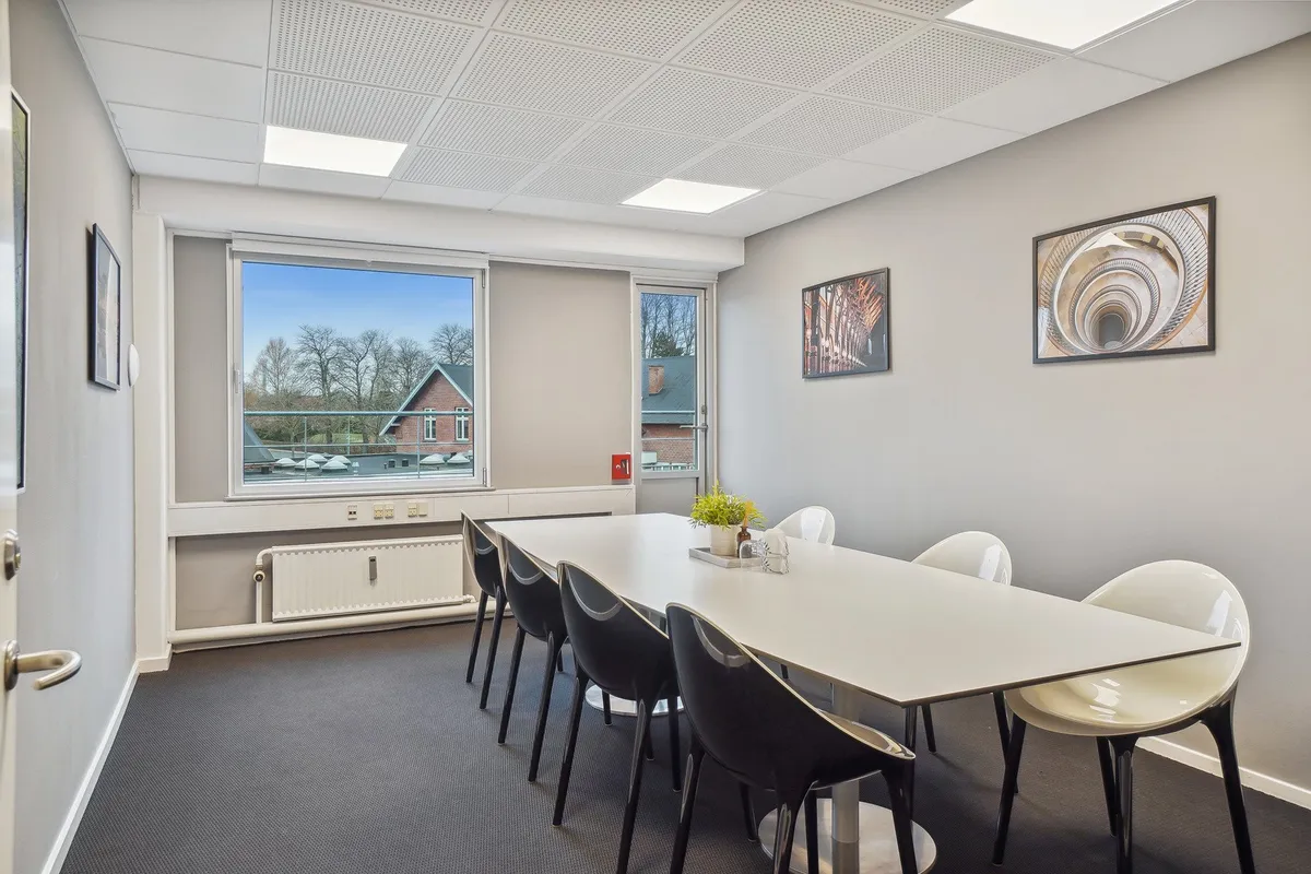 Kontor med langt, rektangulært bord, høje ruder, radiator og tre malerier med spiraler, spiraltrapper og kirke