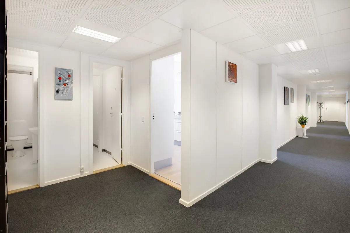 En tom kontorfællesskab med to lukket toiletdør og en lille plante på en høj hvid bord. De hvide vægge er dekoreret med