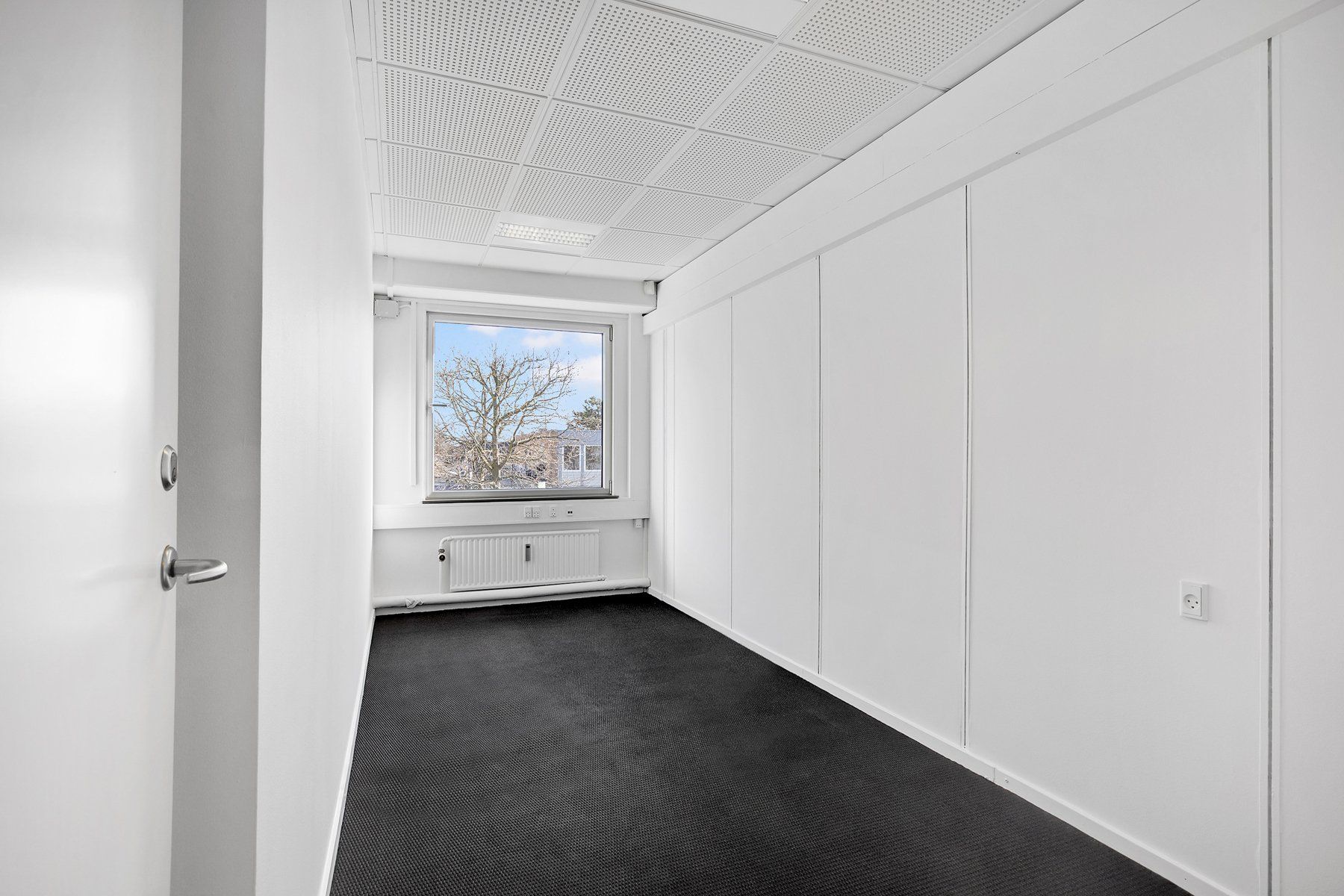 En tom hvid væg med en dør og et vindue i en hvid stue med sort gulv og et hvidt loft