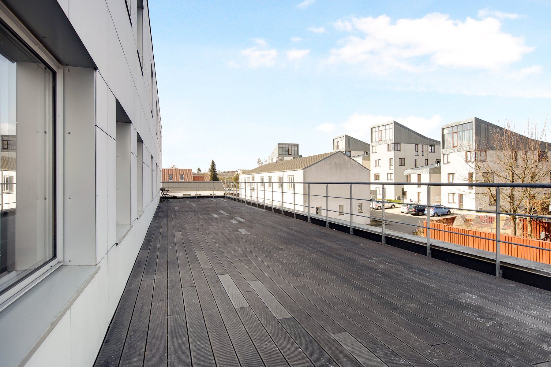Terrasse med udsigt til Taastrup. Moderne bygninger og parkeringsplads med biler i baggrunden.