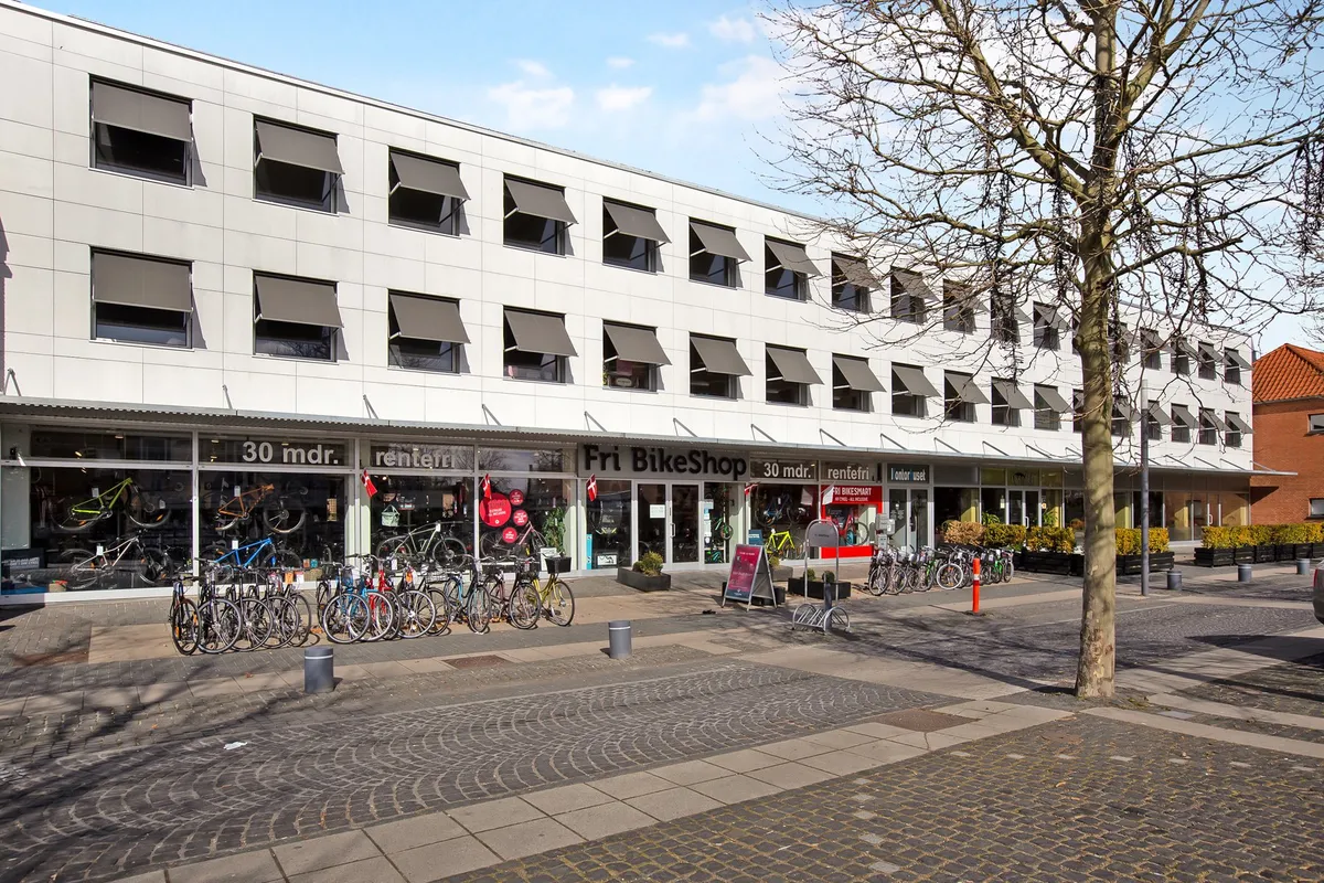Fri BikeShop med mange lejecykler parkeret foran og vinduer med solskærme og flag i Taastrup