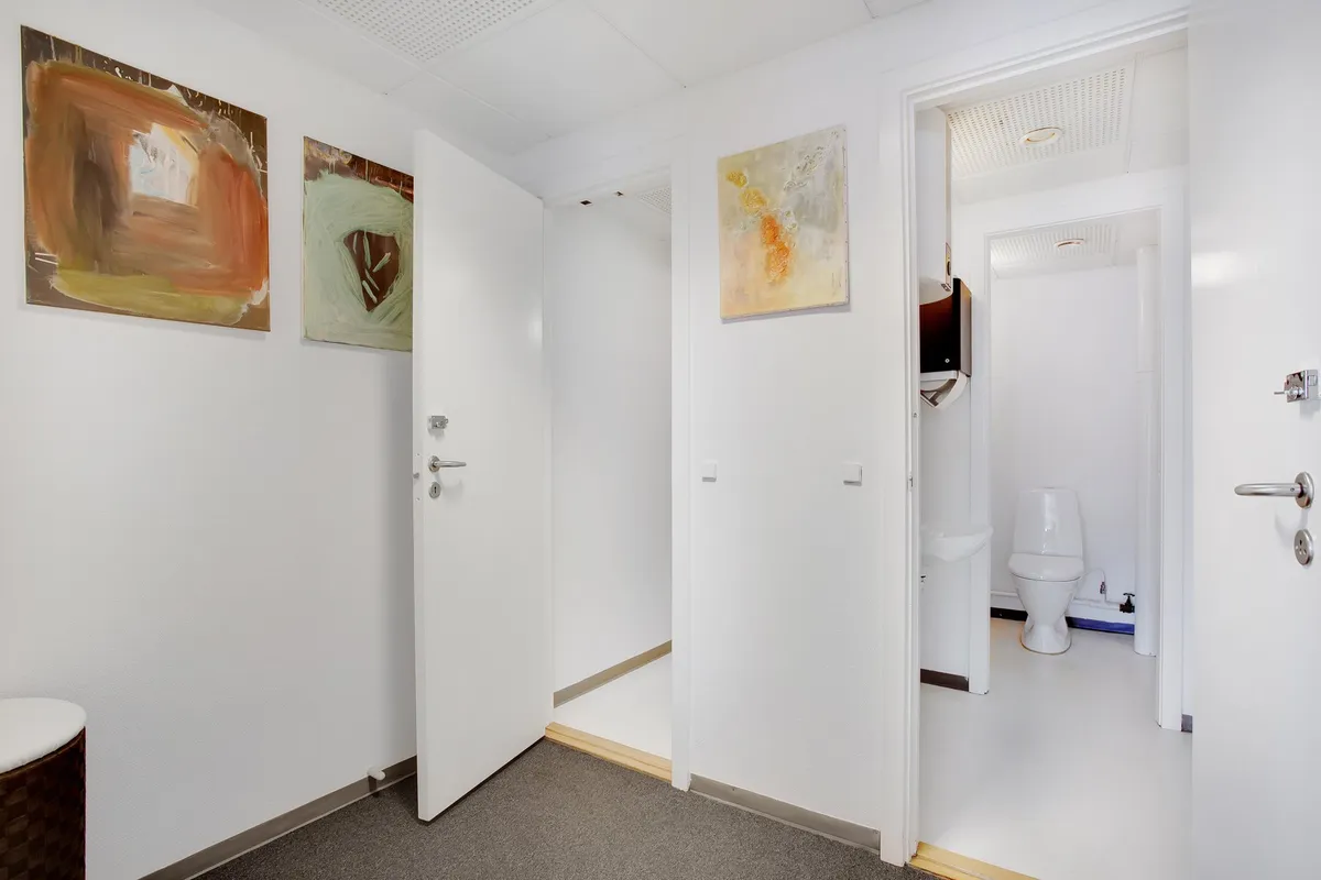 Kontor med toilet og kunstværker på væggen og toilettet med hvid toilet og hvidt toiletpapir