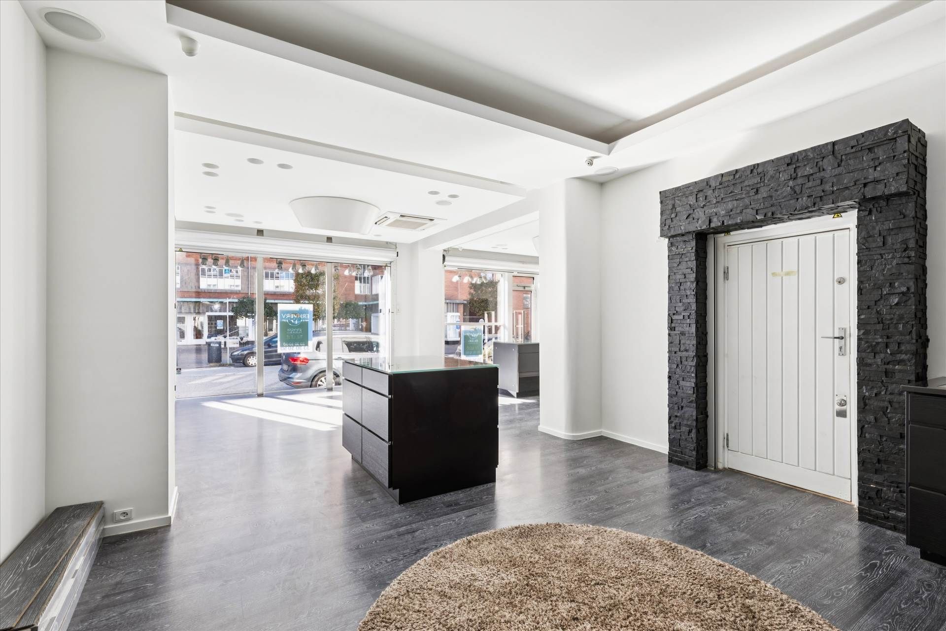 En stor, moderne indgangsdør med gulvbelægning og møbler i sort og hvid, samt en stor sofa i brun og en åben vej med biler