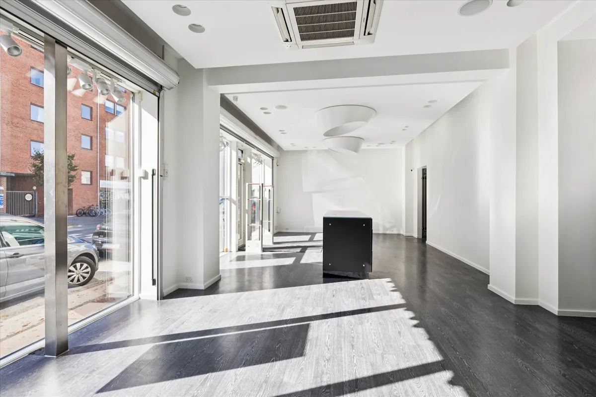 Et moderne og pænt indre lokale med glasdøre og gulvbelægning, hvor der er parkerede biler og en række cykler udenfor