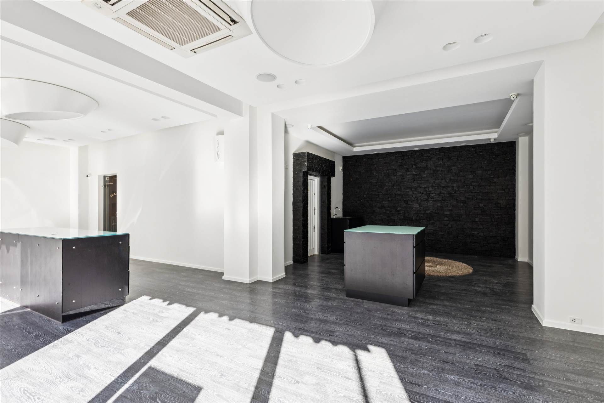 Minimalistisk og funktionel kontor med højt loft, to store sort/grå skriveborde, og et sort og gult murværk.